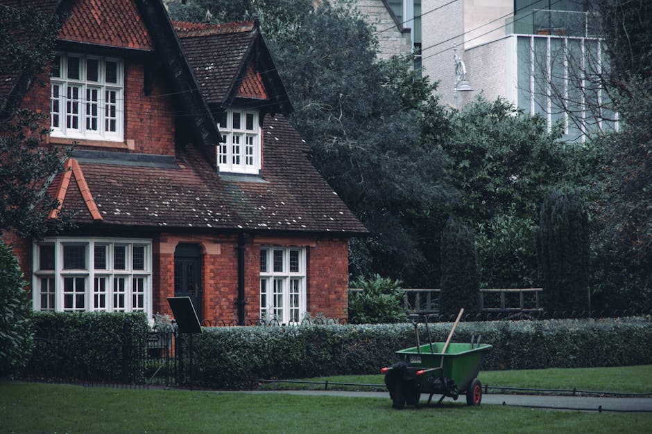 A red brick terraced home with a steep, tiled roof featuring dormer windows and white-framed sash windows. The front garden has a neatly trimmed hedge along the pathway and a well-maintained lawn area